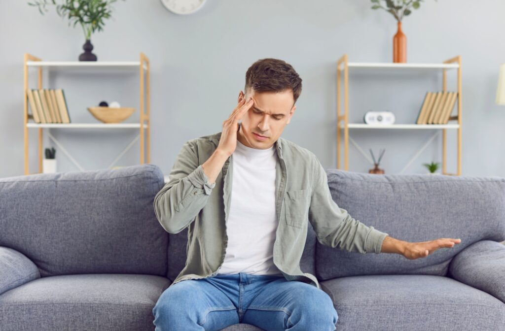 A person sitting on a grey couch rubs their temple during a bout of dizziness.