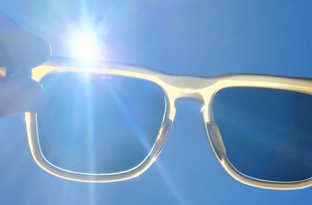A person's hands as they hold a pair of glasses up to the sunny sky.