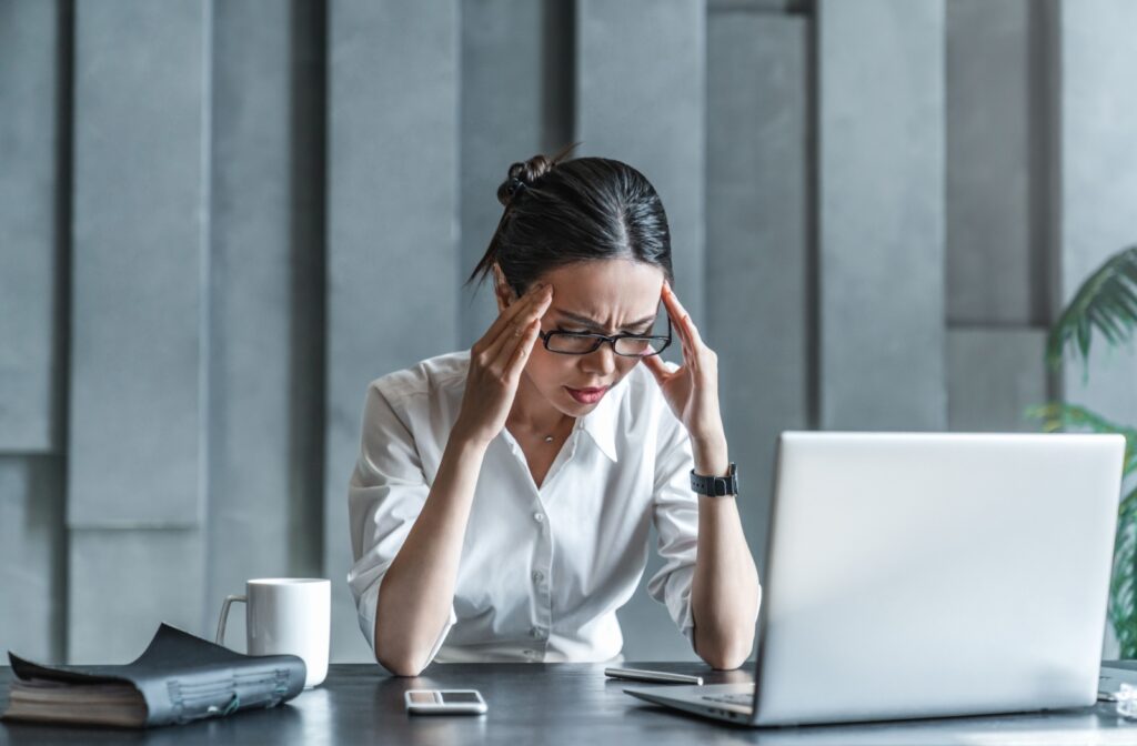 A young professional rubbing their temples at a computer due to a headache.