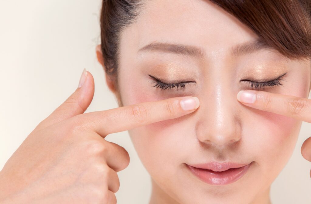 A person gently massaging their lower eyelids with their index fingers after applying a warm compress, helping to unclog their meibomian glands and improve oil flow.