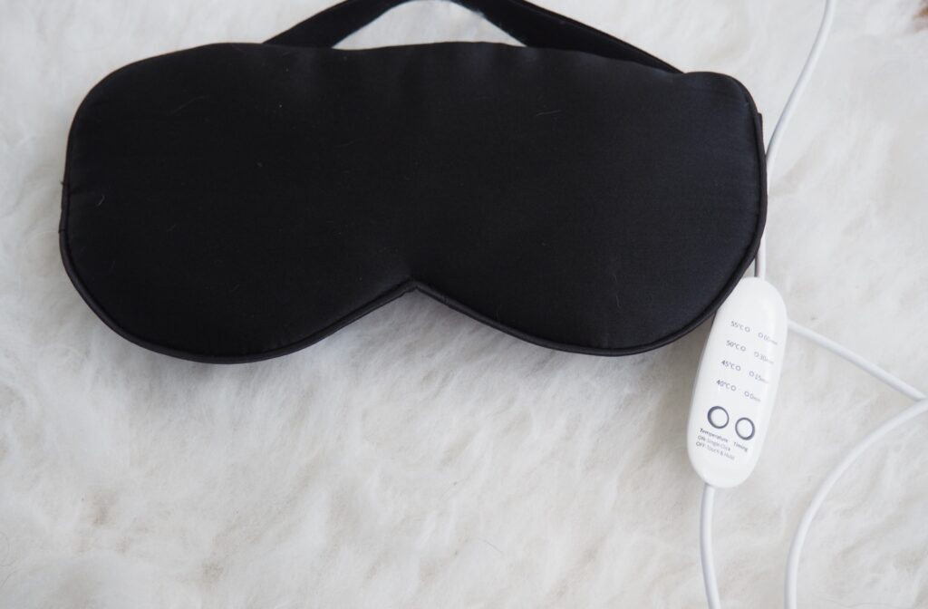 Black heated eye mask with controller on soft white background.